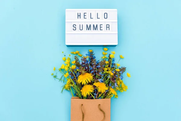 Text Hello Summer on light box and bright bouquet of wildflowers in craft package on blue background. Concept summer time. Top view Flat lay Template for postcard, greeting card