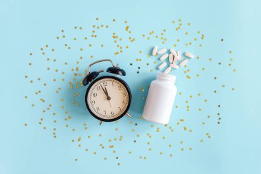 İki hap, beyaz şişe, siyah alarm saati ve mavi arka planda altın yıldızlı konfeti. Insomnia kavramı, uyku sorunları, uyku hapları melatonin alma zamanı. Üst Görünüm Düz yatay Boşluğu Kopyala.