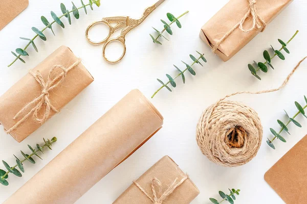 Set of materials for packing holiday gifts. Kraft paper, jute twine, scissors, boxes and twigs of green eucalyptus on white background. Holiday zero waste and eco-friendry concept. Top view Flat lay.
