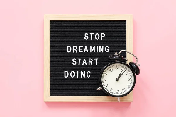 Stop Dreaming Start Doing. Motivational quote on frame letter board and black alarm clock on pink background. Top view Flat lay Concept inspirational quote of the day.