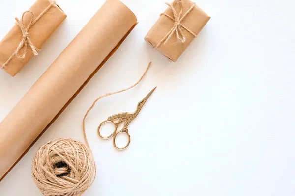 Set of materials for packing holiday gifts. Kraft paper, jute twine, scissors, boxes on white background. Holiday zero waste and eco-friendry concept. Top view Flat lay Copy space.