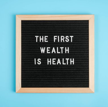 İlk zenginlik sağlıktır. Mavi arka planda siyah harf tahtasından motivasyon alıntısı. Konsept Sağlık ve Tıp, günün ilham verici alıntısıdır..