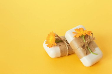 El yapımı doğal sabun. El işi kağıt, kırbaç ve sarı arka planda turuncu takvim çiçekleriyle süslenmiş. Organik kozmetik konsepti. Dizayn için Üst Görünüm Düz Şablonu.