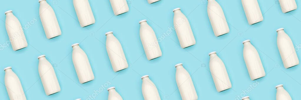 Pattern made with transparent glass bottle of milk on blue background. Flat lay Top view Banner.