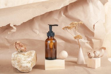Taşın üzerinde kozmetik ürünlerin pompası olan kahverengi cam şişe, tahta geometrik şekiller ve bej kağıt arka planda kurutulmuş çiçekler. Doğal Organik Spa Kozmetik Güzellik Konsepti Ön Görünüm Model.