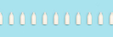 Glass bottles of milk in a row on blue background. Flat lay Top view Banner Copy space. clipart