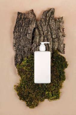 Krem, nemlendirici losyon, şampuan ya da diğer kozmetik ürünleri yeşil yosun ve ağaç kabuğu arkaplanlı beyaz boş şişede. Doğal Organik Spa Kozmetik Konsepti Üst Görünüm.