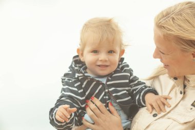 Bekar bir anne, göl kenarında doğal sarı ve beyaz arka planlı bir çocuğu taşıyıp kucaklıyor.