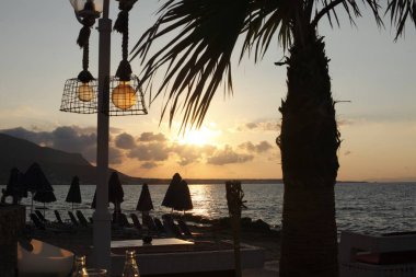 Sonsuz ufku olan inanılmaz sahil günbatımı. Hindistan cevizi ağacı lambaları. Yunanistan 'da popüler bir turizm merkezi olan Girit' te, güzel, kırmızı kadife bir gün batımı gökyüzünde, ahşap lambaların koyu gölgeleri.