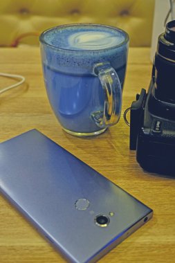 Moda içeceği, mavi latte. Sıcak kelebek bezelye latte çayı ya da mavi spirulina latte ve ahşap masa arkasındaki fotoğraf makinesi manzarası..