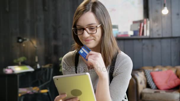 Красивая молодая женщина держит кредитную карту улыбаясь на iPad пьющий кофе Медленное движение выстрел на красную эпопею 8K — стоковое видео