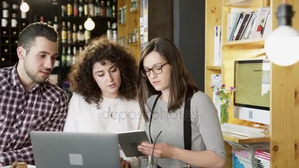 Modny młody biznes drużyna mężczyzny i kobiety, omawianie projektu trzymając Tablet i patrząc na ekran laptopa w Coffee barze wolno ruchu strzał na Red Epic 8 k — Wideo stockowe