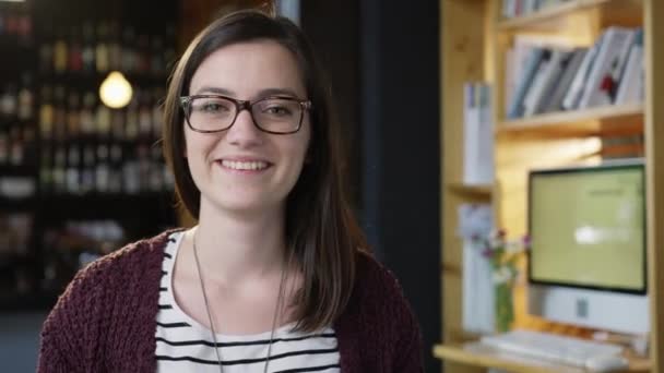Mulher jovem profissional inteligente com óculos sorrindo para a câmera na biblioteca Café Bar Confiança Otimismo Felicidade Liderança Conceito Slow Motion Shot On Red Epic 8K — Vídeo de Stock