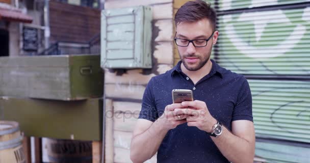 Hübscher junger Mann surft Smartphone lächelnd Millennial Lifestyle im Freien Zeitlupe Schuss rot episches 8k — Stockvideo