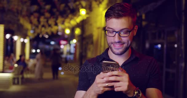 ハンサムな男が笑って現代技術 4 g スマート フォンのメッセージング 4 g 接続ダウンタウン スローモーション撮影赤の壮大な 8 k — ストック動画