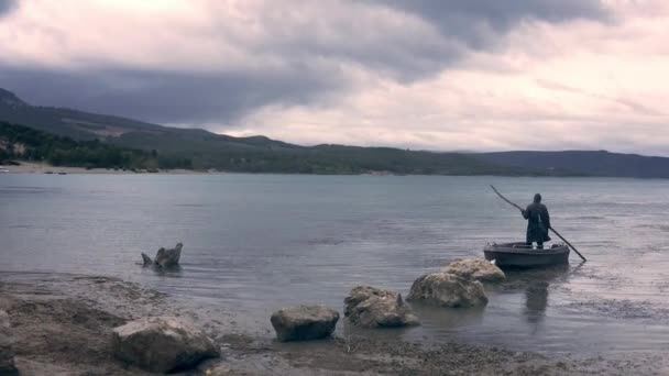 Рыбак в капюшоне, стоящий на пустынном берегу лодки холдинг персонала Конец времен изменения климата Стихийные бедствия Загадка фантазии сказки — стоковое видео