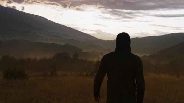 Solitario uomo incappucciato in piedi su campo vuoto a ora d'oro distanza sociale viaggio rallentatore 8k — Video Stock