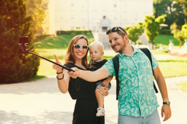 Young family with toddler child making selfie photo on motion camera in park of Europe 