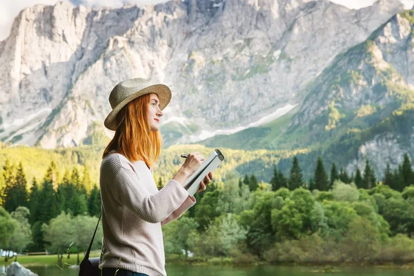 Mujer joven haciendo bocetos o escribiendo en su bloc de notas sobre la naturaleza — Foto de Stock