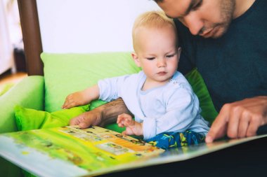 Küçük bir çocuk babasıyla bir ev Interio bir kitap okuyor