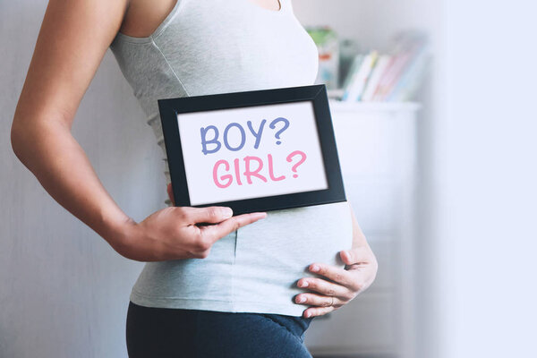 Pregnant woman holds whiteboard with text message - BOY or GIRL?
