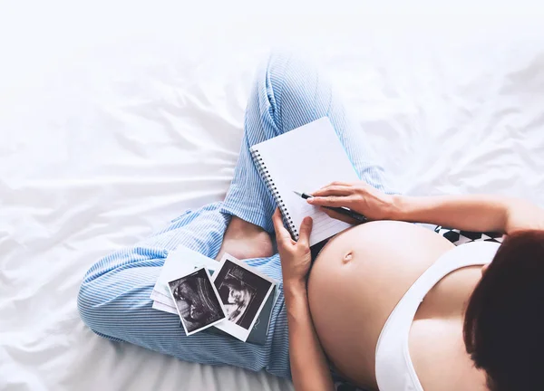 Mujer embarazada toma notas en el cuaderno y la celebración de ultrasonido im — Foto de Stock