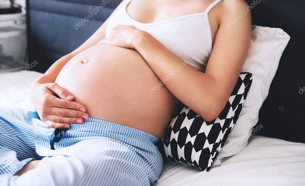 Close-up pregnant woman's belly in bedroom at home.