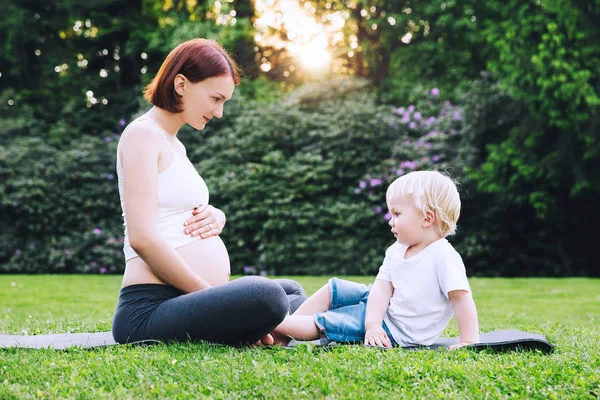 Zwangere vrouw doen yoga en rusten met zoon op de natuur. — Stockfoto