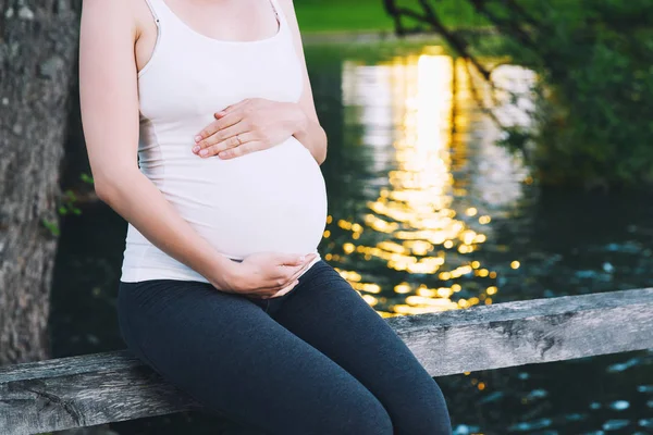 Mulher grávida mantém as mãos na barriga no fundo da natureza — Fotografia de Stock