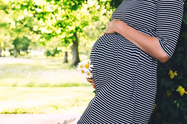 Close-up van zwangere vrouw met bloemen op natuur achtergrond. — Stockfoto