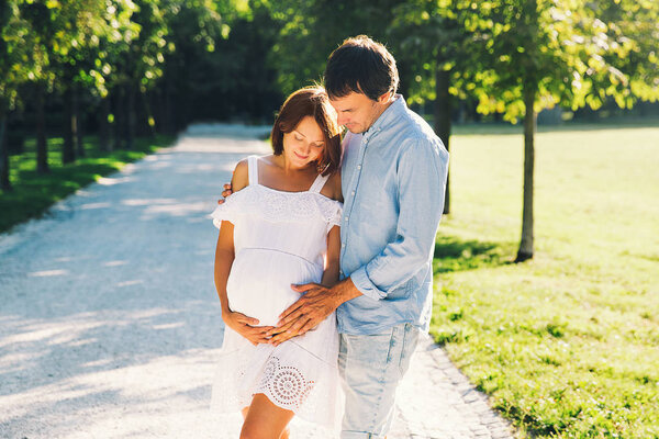 Happy and pregnant couple in love hugging in summer nature. Beautiful pregnant woman and her husband outdoors. Happy family and pregnancy concept.