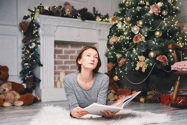 Frau liest zwischen Weihnachtsdeko ein Buch. — Stockfoto