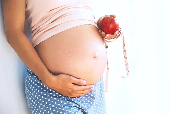 Close up de uma mulher grávida segurando maçã e fita métrica . — Fotografia de Stock