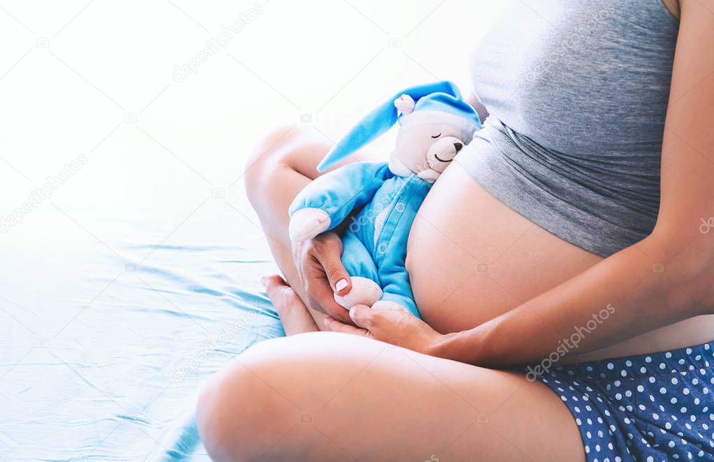 Close-up pregnant woman's belly with teddy toy bear.