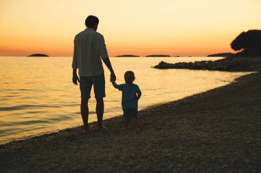 Baba ve oğul deniz tarafından yürüyüş siluetleri geri.
