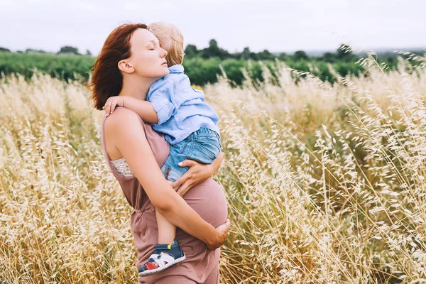 Pregnant woman and son on nature. Mother waiting of a second bab