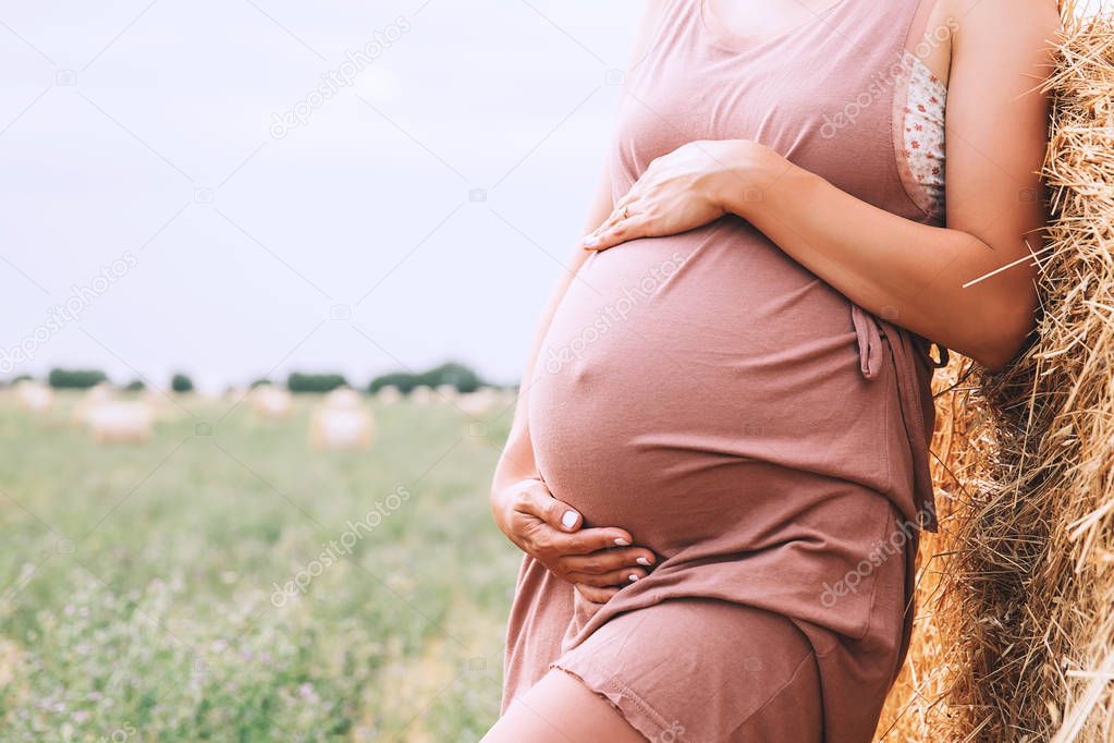 Pregnant woman holds hands on belly on nature background, outdoo