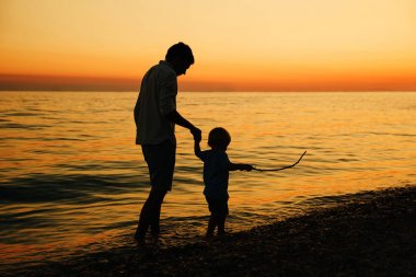 Baba ve oğul deniz tarafından yürüyüş siluetleri geri.