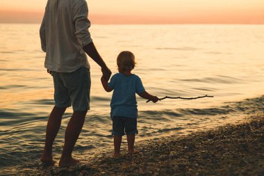 Baba ve oğul deniz tarafından yürüyüş siluetleri geri.