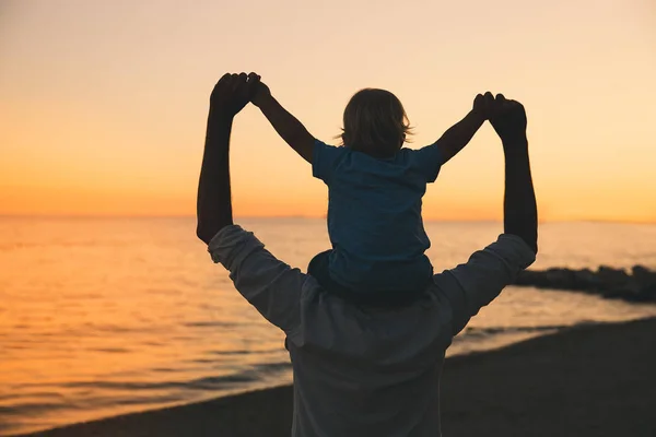 Vader en zoon silhouetten bij zonsondergang op een zee-strand. — Stockfoto