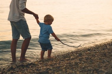 Baba ve oğul deniz tarafından yürüyüş siluetleri geri.