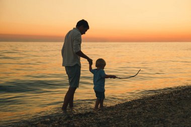 Baba ve oğul deniz tarafından yürüyüş siluetleri geri.