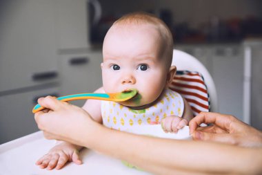Mother feeding little baby with spoon clipart