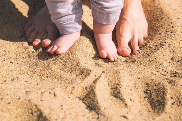 Mãe e pequenos pés de bebê na areia da praia . — Fotografia de Stock