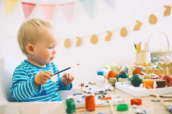 Easter morning. Little children painting eggs. Family preparing for Easter. Paints, felt-tip pens, decorations for coloring eggs for holiday. Creative background for preschool and kindergarten.