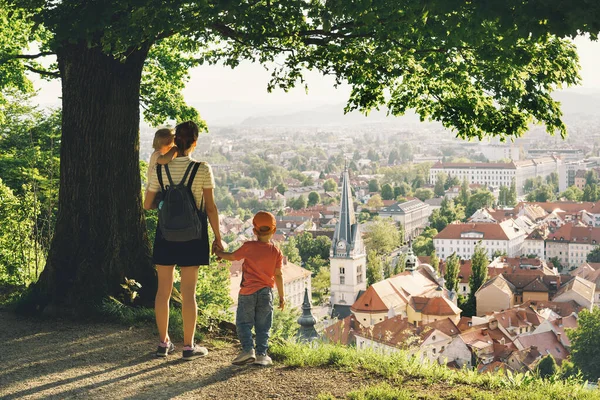 Family on background of Ljubljana, Slovenia, Europe. Woman with two little children looks at panorama of european city from the hill. Mother and kids outdoors at spring or summer time.