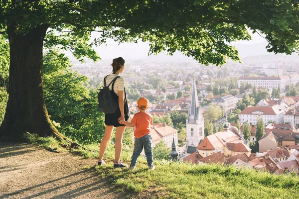 Family on background of Ljubljana, Slovenia, Europe. Woman with her child boy look at panorama of european city from the hill. Mother and kid outdoors at spring or summer time.