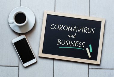 Coronavirus ve Business metni tahtaya yazılmış. Covid-19 - Wuhan Roman Coronavirus pnömonisi. Kahve ve cep telefonlu tebeşir tahtası.