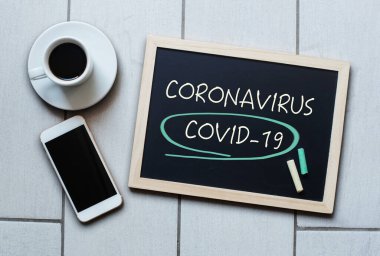 Coronavirus Covid-19 yazı tahtaya yazılmış. Covid-19 - Wuhan Roman Coronavirus pnömonisi. Kahve ve cep telefonlu tebeşir tahtası.