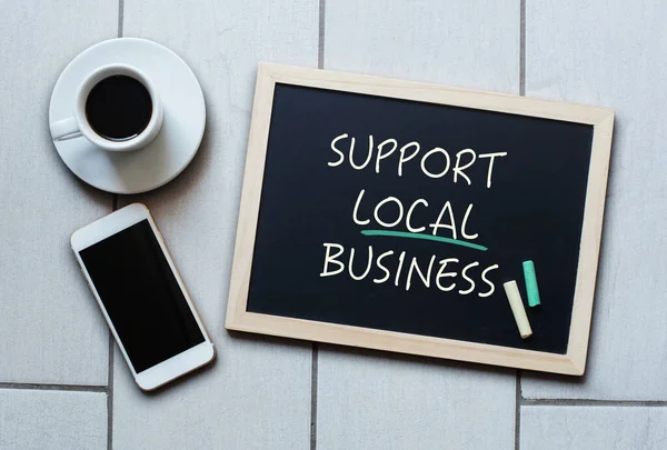 Support Local Business text written on blackboard. Chalk board with coffee and mobile phone.